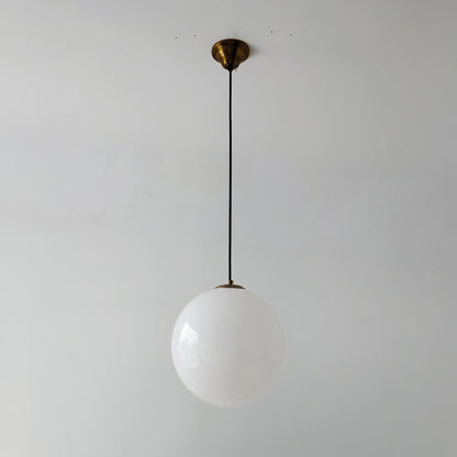 Unlit White mid century style glass globe pendant light with a brass ceiling canopy and black cord against a plain wall.
