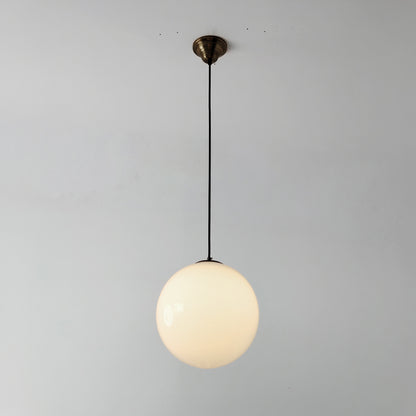 Lit White mid century style glass globe pendant light with a brass ceiling canopy and black cord against a plain wall.